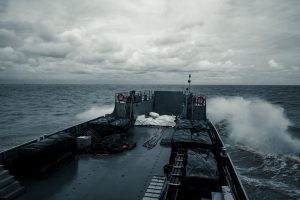 A military ship cruises through choppy ocean waters under a cloudy sky, showcasing naval power.