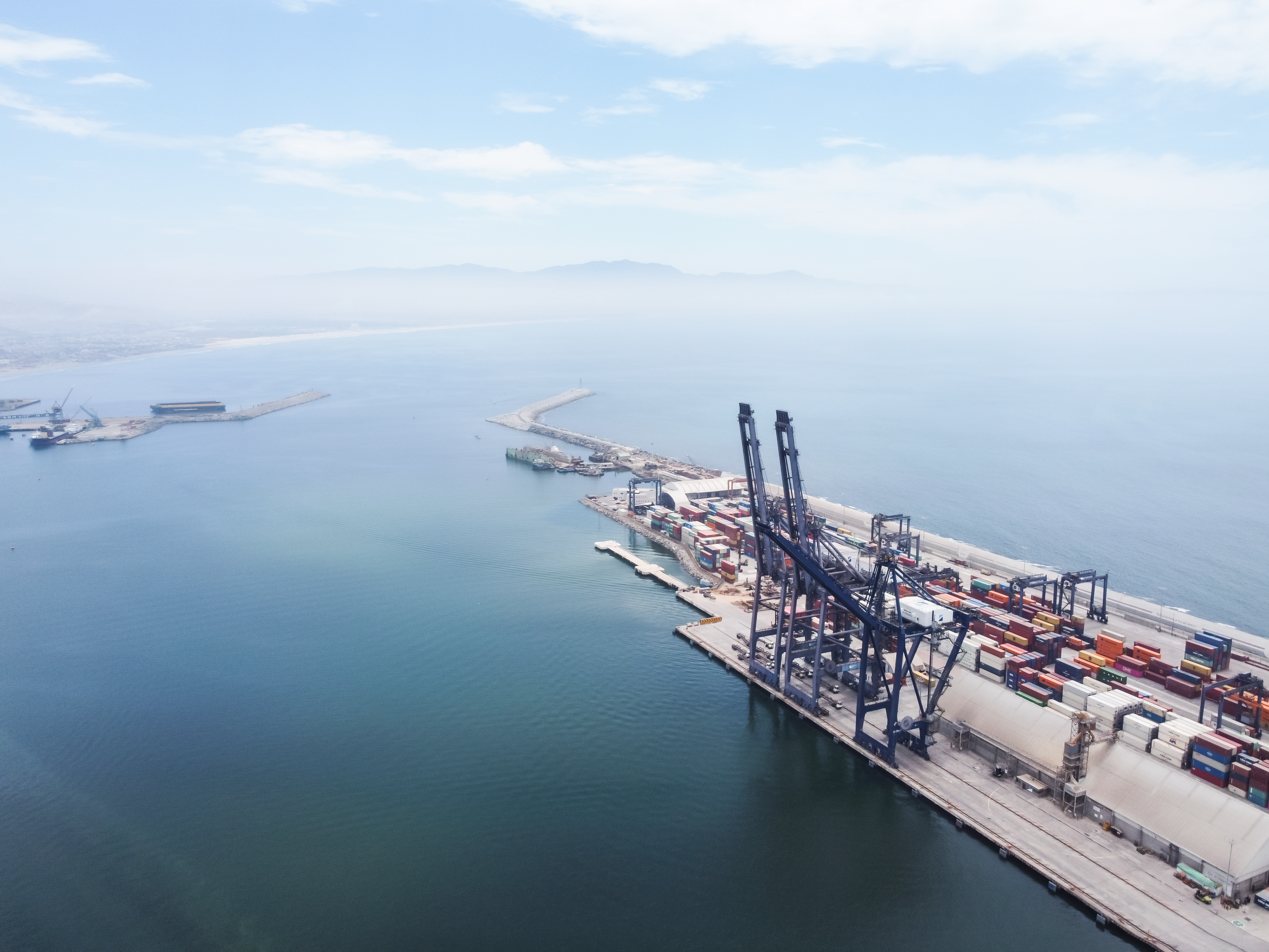 A sweeping aerial shot capturing logistics and container ships at Ensenada Port, Baja California.